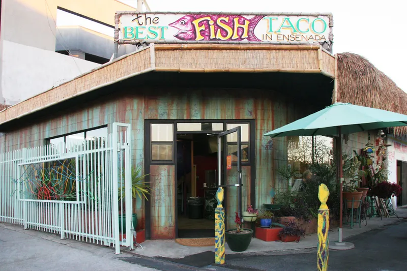 Palapa-roofed corner storefront of Best Fish Taco In Ensenada in Los Feliz, Los Angeles, with its hand-painted fish sign and patio umbrella