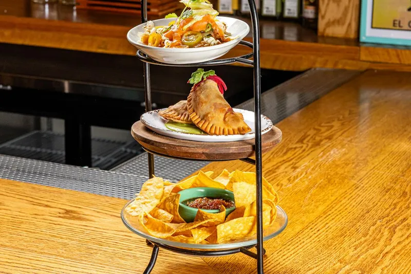 A three-tier stand holding chips and salsa, a filled empanada, and a plated appetizer at Bar Mexicana in New York