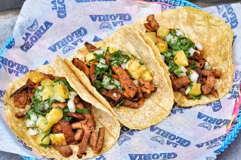 Three tacos served in a blue basket at La Gloria Pearl