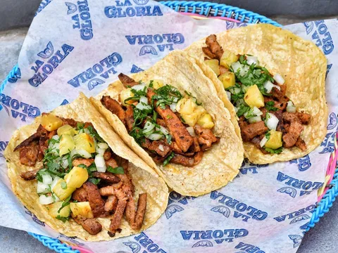 Three tacos served in a blue basket at La Gloria Pearl