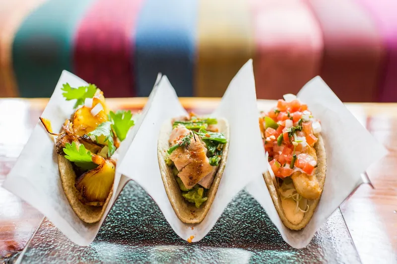 Three tacos in paper holders on a wooden table at Oyamel in Washington, DC