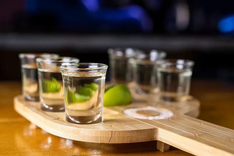 Row of tequila shots with lime on a wooden board at Kompali Taqueria