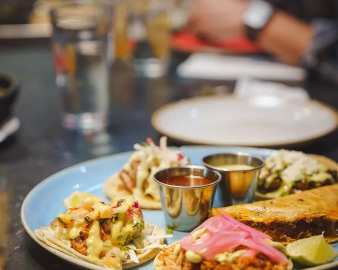A plate of assorted street tacos with dipping salsas and lime at Tacos Tequila Whiskey
