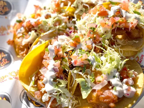 Tray of Baja-style battered fish tacos topped with cabbage, pico de gallo and crema on Baja Cali Fish & Tacos branded paper