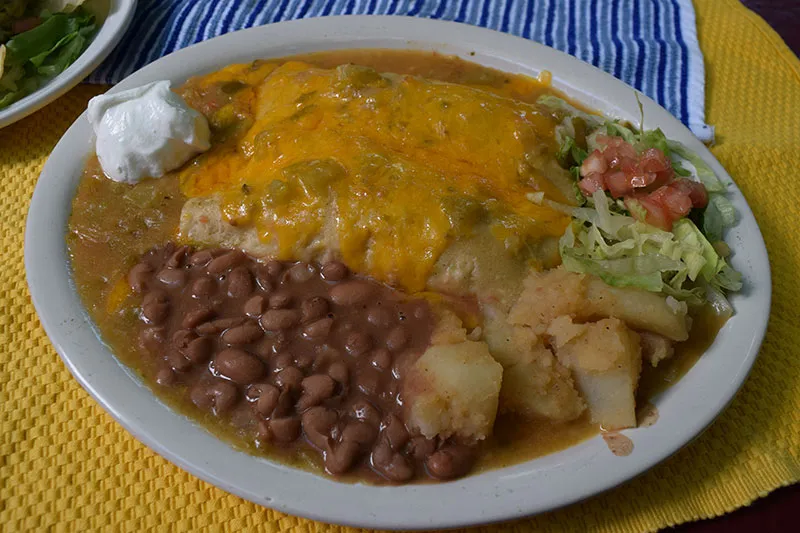Plate of green chile chicken enchiladas smothered in green chile and melted cheese with sour cream, pinto beans and papas at El Patio de Albuquerque