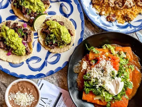 A spread at La Santa Modern Mexican in Raleigh: carne asada street tacos with guacamole on a blue Talavera plate, a chicken-and-rice plate, enchiladas, and refried beans beside a La Santa menu card
