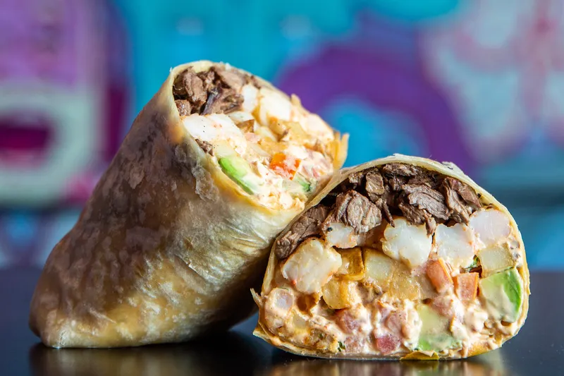 Lucha Libre Taco Shop's Surfin' California Burrito cut in half showing steak, shrimp, fries and avocado