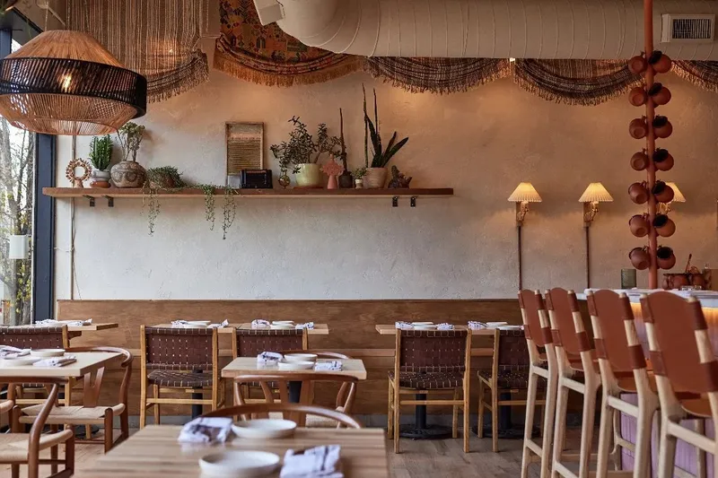 The plaster-walled dining room at Alma Fonda Fina in Denver, with woven-leather chairs, banquette seating and hanging terracotta cups along the bar