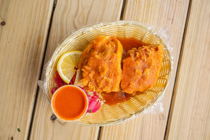 Two tortas ahogadas — birote rolls drenched in red chile sauce — in a basket with a cup of salsa, pickled onions and a lemon slice at Tortas Ahogadas El Chivito in San Antonio