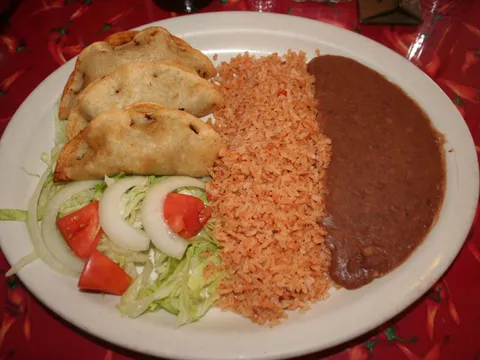 A plate of crispy tacos de carne deshebrada (shredded beef) with Mexican rice, refried beans and a lettuce-tomato-onion salad on Benito's signature red chile-pepper tablecloth in Fort Worth