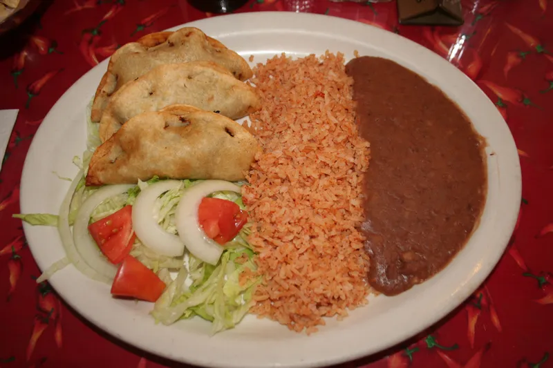 A plate of crispy tacos de carne deshebrada (shredded beef) with Mexican rice, refried beans and a lettuce-tomato-onion salad on Benito's signature red chile-pepper tablecloth in Fort Worth