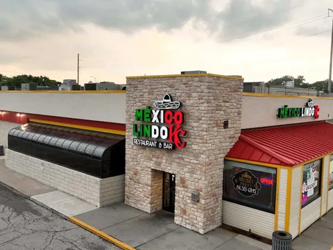 Exterior of Mexico Lindo KC Restaurant & Bar at 1046 W 103rd St, Kansas City, showing the stone facade, red roof and lit 'México Lindo KC Restaurant & Bar' sign with a sombrero logo