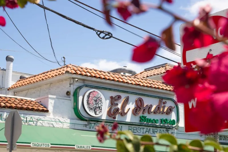 El Indio Mexican Restaurant storefront on India Street with its neon 'El Indio Since 1940' sign, red-tile roof and green awning, framed by bougainvillea