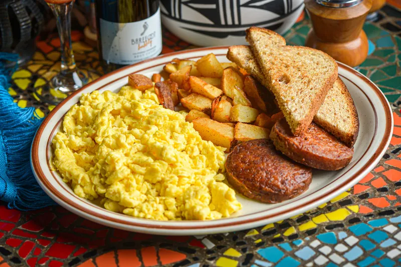 Breakfast plate with scrambled eggs, home-fried potatoes, grilled chorizo sausage and wheat toast on a colorful mosaic-tiled table at Church Street Cafe in Old Town Albuquerque