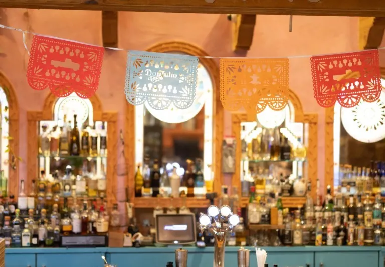 El Pinto's cantina bar with papel picado banners under a beam reading Est. El Pinto 1962