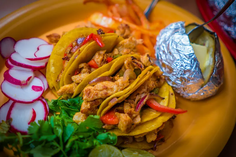Plate of chicken fajita tacos on corn tortillas with sliced radishes, cilantro and a foil-wrapped baked potato at Tacos Chinampa in El Paso