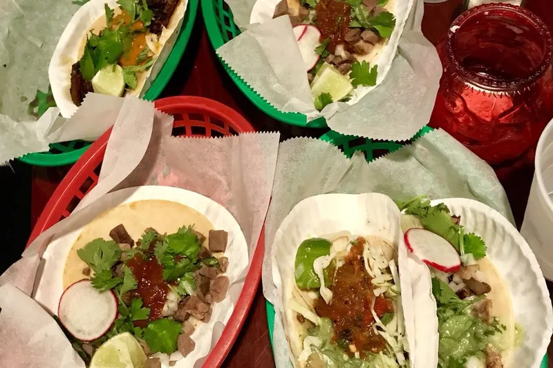 Four soft tacos with steak, cilantro, radish and salsa in red and green baskets on a table at Taqueria Downtown in Jersey City