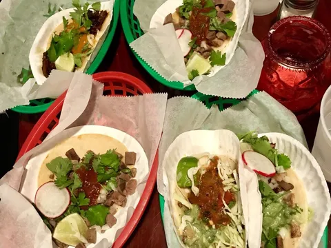 Four soft tacos with steak, cilantro, radish and salsa in red and green baskets on a table at Taqueria Downtown in Jersey City