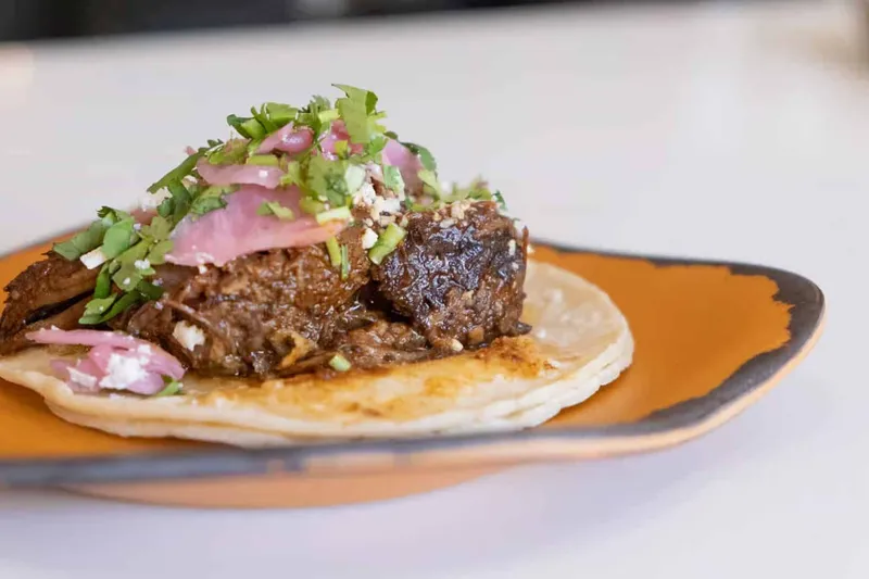 Mas Taco Bar's short rib taco — braised short rib topped with pickled red onion, cotija cheese and cilantro on a soft corn tortilla, served on an amber plate