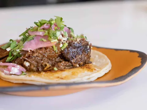 Mas Taco Bar's short rib taco — braised short rib topped with pickled red onion, cotija cheese and cilantro on a soft corn tortilla, served on an amber plate