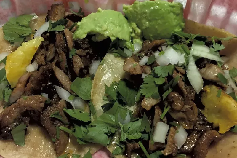 Two street tacos at Taco Gordo in Burlington, piled with grilled pork, chopped onion, cilantro, guacamole, and lime in a paper-lined basket