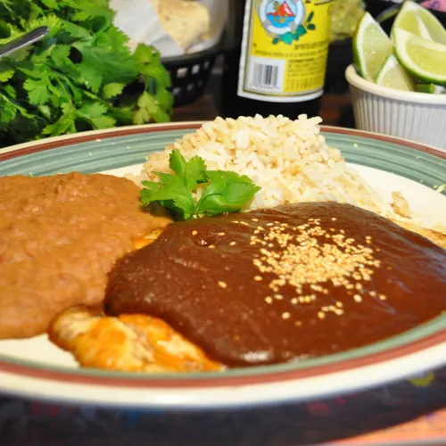 Mole poblano con pollo — chicken breast under dark poblano mole sauce topped with sesame seeds, with Mexican rice and refried beans at Guajillo's