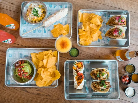Overhead spread of tacos, tortilla chips, guacamole, elote and salsas on metal trays at Coyo Taco