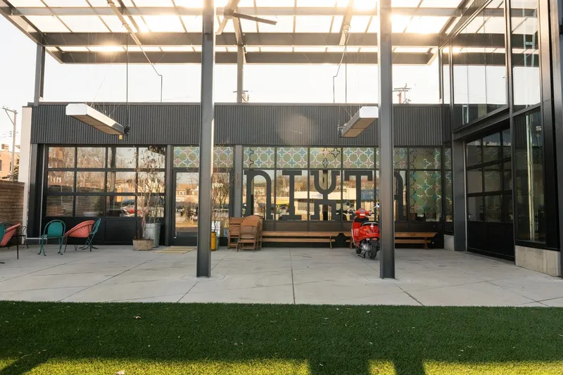 Exterior patio of Nixta in St. Louis at dusk, with the NIXTA name across the tiled storefront windows, wooden benches, and a red scooter parked under a steel canopy