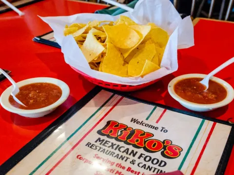 Basket of tortilla chips with two bowls of red salsa beside a Kiko's Mexican Food Restaurant & Cantina table menu